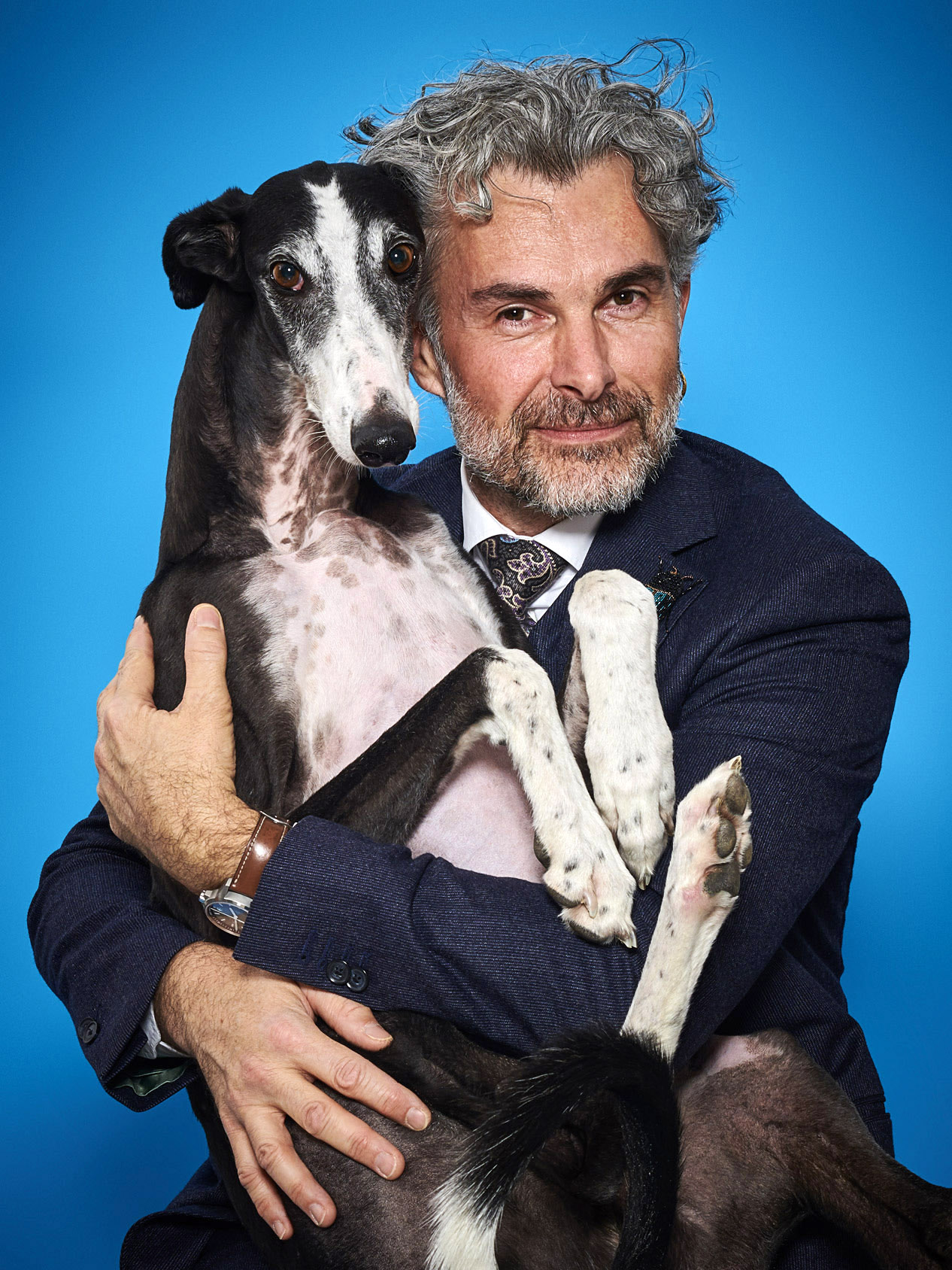 Beitragsbild People,Person mit Hund im Arm, blauer Hintergrund, schmunzelt in die Kamera, Portrait Fotografie